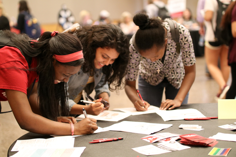 Students smiling and writing on paper at a career event